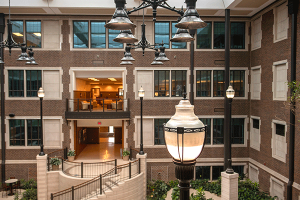 Interior of an expansive atrium area in a brick, multi-story building with a large lamppost visible in the lower right corner and office windows and entryways arranged symmetrically on the far side. 